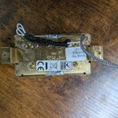Zadní strana elektrického snímače v zlatém kovovém provedení. Na povrchu je bílá nálepka s nápisy 57/08 TM, TREBLE a číslem 3197. Vedle ní je vyražen…