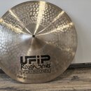 Kladivovaná kovová činely v přirozené zlatavé barvě. Na povrchu je černý nápis UFIP Rough Series EARCREATED CYMBALS a menší štítek s textem 18" CRASH…