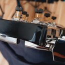 Detailní záběr na chromované ladičky s černými knoflíky. Na horní části je vidět černý plastový kryt, který zakrývá část mechanismu. Na komponentech…