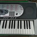 Šedý digitální klavír s bílými a černými klávesami. Na ovládacím panelu jsou nápisy TONE, RHVTHM, SONG BANK, TOUCH RESPONSE a logo midi. V pravém hor…