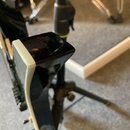 Detailní pohled na spodní část těla elektrické kytary v černé barvě s bílým lemováním. Nástroj je umístěn na černém stojanu. Na povrchu jsou vidět od…
