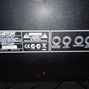 Detail zadní strany černého akustického kytarového komba. Na bílém štítku je uveden název KUSTOM, MODEL SIENNA30 ACOUSTIC GUITAR AMPLIFIER a SERIAL N…