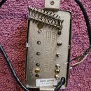 Fotografie znázorňuje zadní stranu elektrického snímače s kovovým krytem a pružinou. Na povrchu je logo a nápis Seymour Duncan a text Made in USA. V…