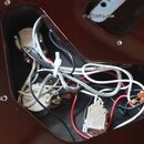 Fotografie zachycuje vnitřek vyfrézované dutiny v tmavě hnědém lakovaném dřevě elektrokitary. Uvnitř jsou vidět zapojené potenciometry, bílé a černé…