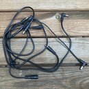 Černý audio kabel s několika konektory, položený na dřevěném povrchu. Na kabelu je viditelný nečitelný bílý nápis. Povrch kabelu a konektory vykazují…
