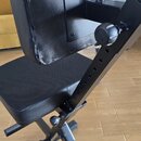 Černá polstrovaná židle s opěradlem a nastavitelným kovovým rámem. Na zadní straně opěradla je připevněný černý držák s dvěma plastovými knoflíky. Po…
