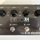 Šedý efekt pedál s nápisem DITTO X4 LOOPER a logem tc electronic. Zařízení má čtyři stoupací spínače označené jako LOOP 1, LOOP 2, STOP a FX. V horní…