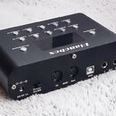 Černý elektronický přístroj s nápisem Pianobox. Na horní straně se nachází displej a řada ovládacích tlačítek s popisky jako Drum/Sound, Volume-10, V…