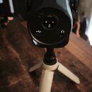 Černý cylindrický přístroj umístěný na malém bílém stativu. Na zadní straně jsou vidět konektory: USB port s ikonou, XLR vstup a jack konektor s ikon…