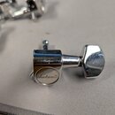 Detailní pohled na jeden chromovaný ladicí kolík kytary. Na kulaté části s nápisem je viditelné logo Jackson®. Povrch vykazuje drobné škrábance a zná…