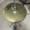 Zlatý kovový činel s koncentrickým žebrováním, umístěný na chromovaném stojanu. Na povrchu je černý nápis METEOR a nad ním logo MEINL. V pravé části…