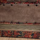 Detailní pohled na část akordeonu s červeným a modrým ornamentálním vzorem. Horní část je zakryta hnědým koženým nebo syntetickým krytem připevněným…