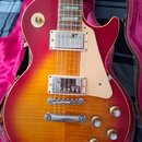 Elektrická kytara s trupem v červeno-žlutém sunburst provedení a hmatníkem z tmavého dřeva. Na světlém pickguardu je svisle napsán text 1960. Nástroj…