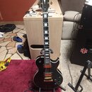 Černá elektrická kytara s tvarem single-cutaway, zlatým hardwarem a hnědým hрифem. Na hlavě je bílý nápis Harley Benton a pod ním značka HB. Kytara m…