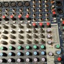Detailní pohled na ovládací panel mixážního pultu s modrým povrchem. Na panelu je vidět logo exicon a nápis 24-BIT DIGITAL EFFECTS PROCESSOR. Jsou zd…