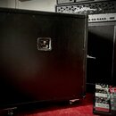 Zadní strana černého kytarového komba s povrchem z texturovaného vinylu, umístěná na kolečkách. Uprostřed je umístěn kovový štítek s nápisem "Marshal…