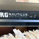 Detailní pohled na horní část černé klávesové pracovní stanice. Na povrchu je bílý nápis KORG NAUTILUS MUSIC WORKSTATION a menší text „Apparaten skal…