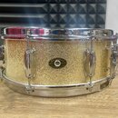 Zlatý snare drum s glitrovým povrchem a chromovanými obručemi a mechanismy. Uprostřed korpusu je oválný štítek s nápisy „Slingerland“, „QUALITY DRUMS…