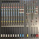 Šedý mixovací pult s vícevstupovými kanály a posuvníky. Na horní části je vidět nápis ALLEN&HEATH a označení modelu PA12. Zařízení obsahuje řadu bare…