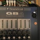 Míchací pult značky Soundcraft, model GB 4. Horní panel je tmavě šedý s bílým nápisem a logem výrobce. Jsou vidět faderové posuvníky s označením GRP1…