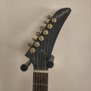 Fotografie zachycuje hlavu elektrické kytary v černé barvě. Na špičce hlavy je bílý nápis Epiphone. Nástroj má šest zlatých ladiček a hnedík z tmavéh…
