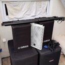 Sada černých textilních krytů na reproduktory, z nichž dva mají bílý nápis YAMAHA s logem. Mezi nimi je umístěn bílý perforovaný kovový kryt reproduk…