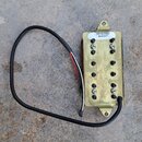 Fotografie znázorňuje elektrický snímač s kovovým krytem v zlaté barvě a černými póly. Na horní části je bílá nálepka s nápisem DP151FBK 849357. Na p…