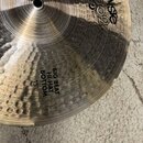 Detailní pohled na kovový činel s kovaným povrchem. Na povrchu je nápis Paiste 2002 s doplňkem DARK a dále text BIG BEAT HI-HAT BOTTOM 15". Povrch vy…