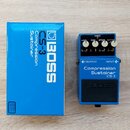 Modrý kompresor značky BOSS, model Compression Sustainer CS-3. Pedál má čtyři ovládací knoflíky s popisky LEVEL, TONE, ATTACK a SUSTAIN, červenou kon…