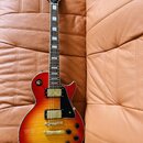 Elektrická kytara s trupem v červeno-žlutém sunburst provedení a černým hmatníkem s bílými vložkami. Na hlavě je bílý nápis Epiphone a logo s textem…