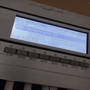 Detailní záběr na displej a ovládací tlačítka klávesového nástroje. Na modrém displeji je vidět text COMBI 1.1:Play, Combination:Combi Select, Bank:…