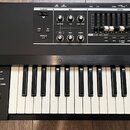 Digitální klavír v černém provedení s dřevěnými bočními panely. Na ovládacím panelu jsou viditelné nápisy D-BEAM, EFX (OVERDRIVE, TONE, COMPRESSOR),…