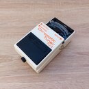 Bílý kytarový pedál s černým spínacím tlačítkem, na kterém je vyražen nápis BOSS. Na horní části je červeným a černým textem uvedeno Chromatic Tuner…