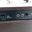 Detail zadní strany hnědého komba s černým ovládacím panelem. Na panelu je napájecí konektor s nápisem 230VAC 50Hz a varovný trojúhelník s textem 100…
