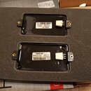 Dva černé elektrické snímače v pěnovém podložním materiálu. Horní snímač má štít s nápisy EMG-57, MADE IN USA, 4550 01, (21)4597784 a 10/25/2024. Dol…