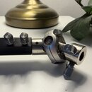 Detailní pohled na kovový spojovací mechanismus s kloubem, který je připevněn k černé hranaté tyči. Mechanismus je vyroben z anodizovaného hliníku st…