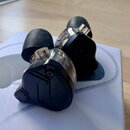 Dva párové špunty do uší s černými silikonovými nástavci a průhlednými plastovými kryty. Na černém plastovém těle je vyražen nápis 10 HYBRID TECHNOLO…