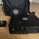 Černý basový zesilovač s nápisem DARKGLASS ELECTRONICS a označením MICROTUBES. Na horní ploše i na přiložené černé brašně je bílé kruhové logo. V pop…
