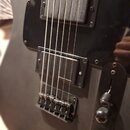 Černá elektrická kytara s matným povrchem a černým pickguardem. Má dva humbuckery, přičemž na spodním je čitelný nápis Seymour Duncan. Nástroj je vyb…