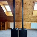 Dva černé reproduktory s vysokými, štíhlými sloupci. Spodní části jsou v podobě hranatých subwooferů, na kterých je umístěno logo Yamaha. Povrch repr…