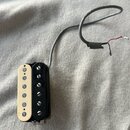 Kytarový snímač s černým plastovým rámečkem a krémově bílým krytem s šesti viditelnými póly. Ze snímače vede šedý kabel s odkrytými červeným a černým…