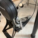 Černý elektronický basový pedál s nápisem Roland a nečitelným textem vedle. Pedál je vybaven kovovou mechanikou s nápisem IRON COBRA 200 a logem TAMA…