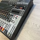 Šedočerný mixážní pult s kovovým chassis a množstvím potenciometrů, posuvníků a konektorů. Na horní části je nápis XENYX X1832USB, pod ním text 16-IN…