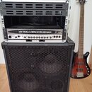 Fotografie zobrazuje basovou kytaru, basový kombozesilovač a rackové pouzdro. Na hlavě kytary je nápis Gallien-Krueger, tělo má červenohnatý sunburst…