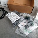 Fotografie zobrazuje sadu příslušenství k hudebnímu zařízení, která obsahuje černý USB kabel a několik malých plastových komponent v originálních prů…