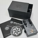 Kytarový efekt pedál stříbrné barvy s černými ovládacími knoflíky a nápisy MICROTUBES X, Darkglass Electronics - MADE IN FINLAND. Vedle pedálu je čer…