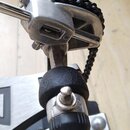 Detailní záběr na mechanismus bicího pedálu s řetízkovým pohonem. Konstrukce je kombinací kovových stříbrných částí a černých plastových či gumových…