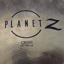 Detailní záběr na kovový činel s viditelným broušením povrchu. Uprostřed je černý nápis PLANET Z v kruhu a pod ním text CRASH 16"/40 cm. Povrch vykaz…