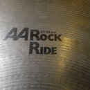 Detailní pohled na kovový činel s viditelným broušením povrchu. Na čineli je černý nápis „A4 Rock RIDE“ a pod ním označení velikosti „21"/53 cm“. Ve…