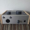 Šedý audio interface s dřevěnými bočními panely. Na zadní straně jsou nápisy 48V, INST, INPUT, VOLUME a HEADPHONES, dva přepínače, jeden regulační kn…